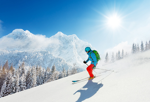 Free-ride skier in fresh powder snow running downhill in beautiful Alpine landscape. Blue sky on background. Free space for text