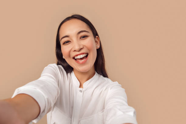 freestyle. młoda kobieta w koszuli stojącej odizolowanej na bage robienia selfie na smartfonie śmiejąc się szczęśliwym zbliżeniowym - selfie zdjęcia i obrazy z banku zdjęć