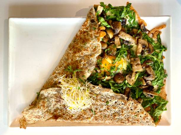 French Buckwheat Crepe with an Egg, Mushrooms and Baby Spinach High angle closeup view of a buckwheat crepe filled with cooked sauted mushrooms, alfalfa sprouts, a fried egg and sliced raw baby spinach on a white ceramic plate savory food stock pictures, royalty-free photos & images