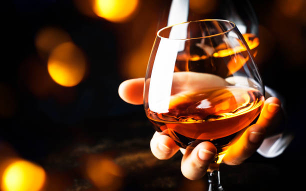 French glowing cognac glass in hand on the dark bar counter background, copy space, selective focus French glowing cognac glass in hand on the dark bar counter background, copy space, selective focus calvados stock pictures, royalty-free photos & images