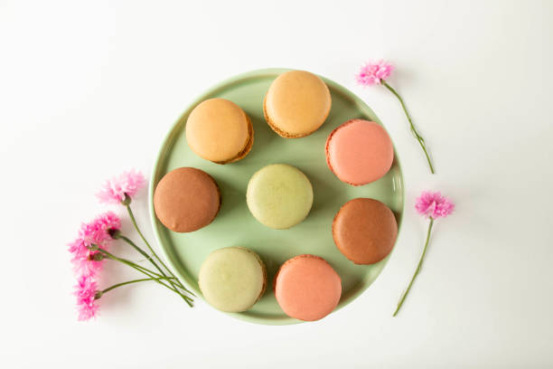 French macaroons on a round plate surrounded by flowers stock photo