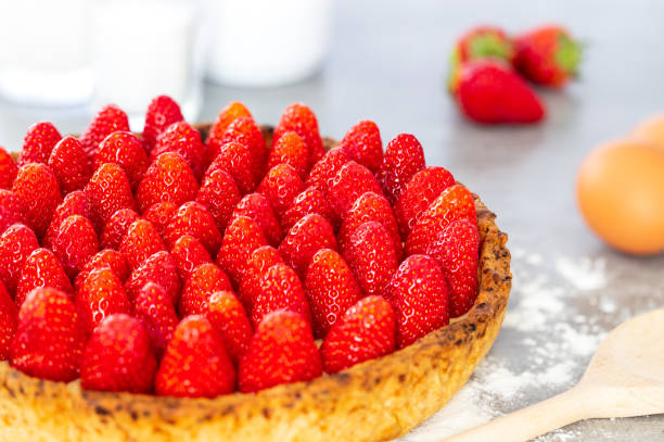 French strawberry tart with sugar, spoon and eggs on a grey background with flour. stock photo