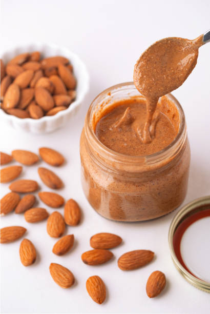Fresh almond butter in a glass jar with raw almonds Small jar of fresh organic almond butter with a spoon dripping into the jar almond butter stock pictures, royalty-free photos & images