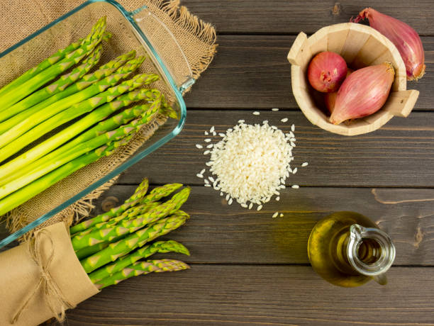Fresh Asparagus on the table along with ingredients such as heap of rice, shallots and extra virgin olive oil, flat lay still life, vegetarian asparagus recipe stock photo