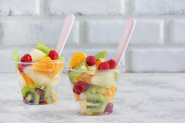 Fresh Assorted Fruit Salad in Takeaway Plastic Cup. Low Calorie Healthy Breakfast on Kitchen Table. Ready to Eat Colorful Vegan Lunch. Ripe Orange, Kiwi Chopped Apple and Raspberry Glass stock photo
