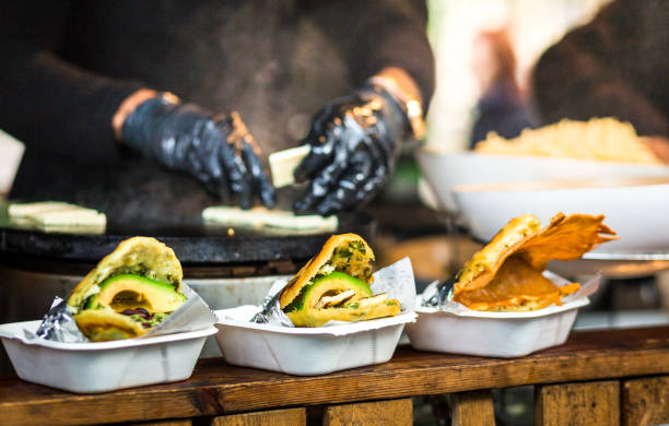 Fresh avocado wraps for sale at vegetarian stall at food market Close up color image depicting freshly made avocado wraps on display on a wooden counter and for sale at an outdoor food market - Borough Market in London, UK. Focus is on the avocado wraps in the foreground, while the chef preparing the sandwiches is defocused in the background. Room for copy space. food state stock pictures, royalty-free photos & images