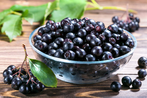 Fresh black chokeberry on plate on wooden background. stock photo