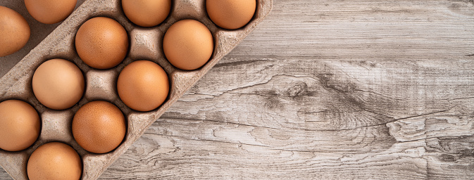Top view of fresh brown chicken eggs in a kraft paper egg carton on wooden table background.