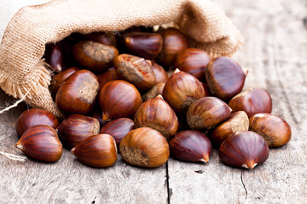 fresh  chestnuts in sack bag on the old wooden table fresh  chestnuts in sack bag on the old wooden table chestnut food stock pictures, royalty-free photos & images