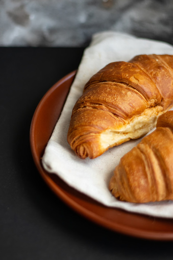 Fresh baked croissants on a clay plate on a dark background