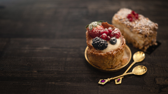 Desserts with custard cream and berries at wooden table with golden spoons. Selective focus, copy space