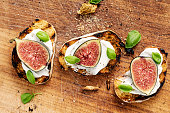 Overhead view of a selection of fresh figs with ricotta cheese, on toasted baguette with torn basil leaves. Colour, horizontal with some copy space.
