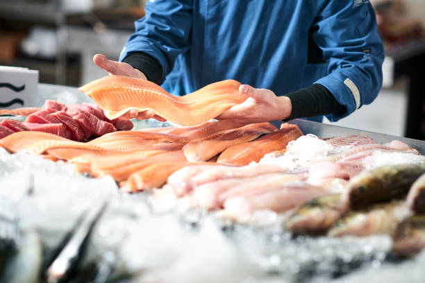 Fresh fish in a fishshop A young male shop assistant in a fishshop saling fresh fish seafood stock pictures, royalty-free photos & images