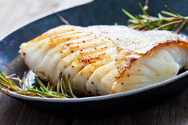 Fresh fried Atlantic cod with rosemary in a frying pan stock photo