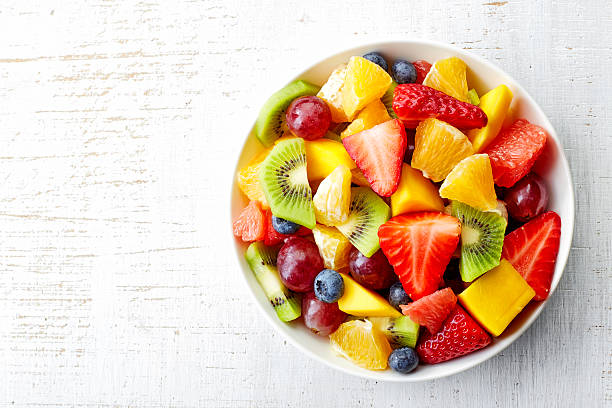 Fresh fruit salad Bowl of healthy fresh fruit salad on wooden background. Top view. fruit stock pictures, royalty-free photos & images