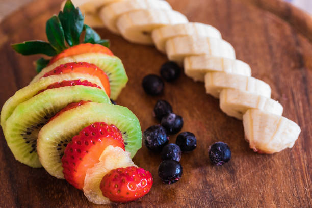 Fresh fruits on wooden plate, strawberry, chokeberry, banana and kiwi stock photo