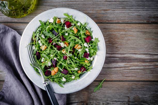 Fresh green salad with arugula, beets, walnuts and feta cheese Fresh green salad with arugula, beets, walnuts and feta cheese on wooden background arugula stock pictures, royalty-free photos & images