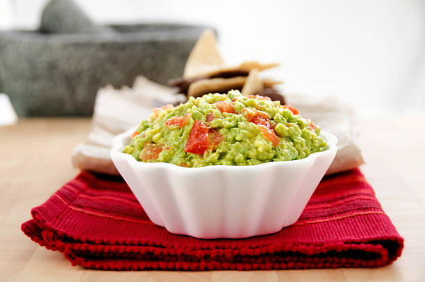 Fresh Homemade Guacamole (Horizontal) Fresh homemade guacamole served with white and blue corn tortilla chips. Mexican stone mortar and pestle (molcajete and tejolote) visible in the background. Selective focus on guacamole. guacamole stock pictures, royalty-free photos & images