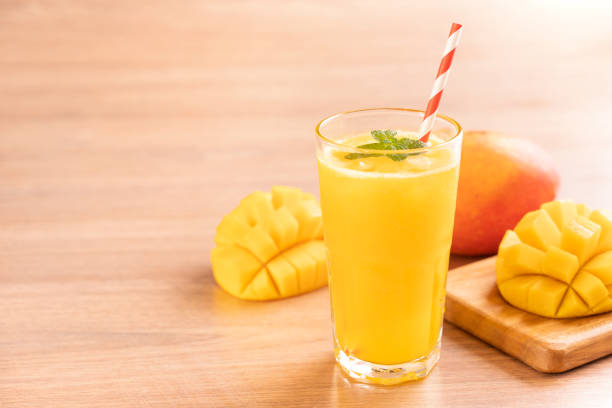 Fresh mango juice with beautiful chopped pulp flesh and straw on bright wooden table background. Tropical fruit design concept. Fresh mango juice with beautiful chopped pulp flesh and straw on bright wooden table background. Tropical fruit design concept. Close up, copy space. mango smoothie stock pictures, royalty-free photos & images
