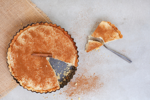 Traditional South African milk tart freshly baked and in tin. Mottled grey and rustic surface with copy space