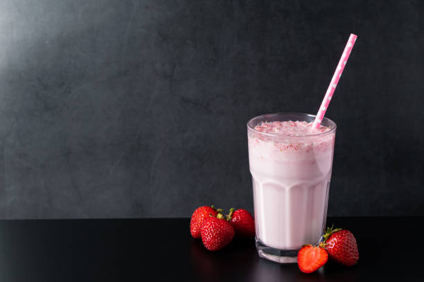 Fresh milkshake with strawberries on black background. Summer drink with a straw in a glass. Place for text. stock photo