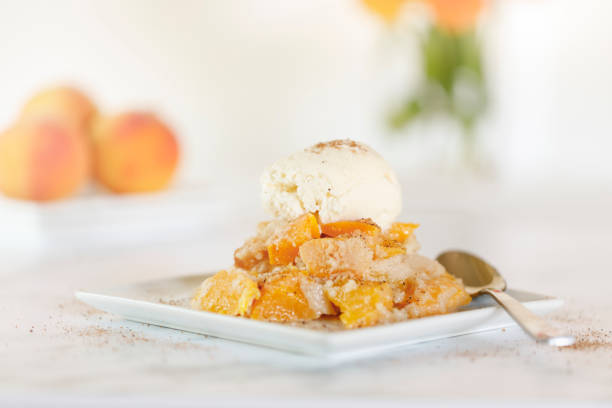 Fresh peach cobbler with vanilla ice cream on a white plate with spoon stock photo
