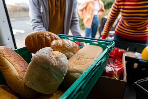 Close up of loaves of bread in a van being delivered to a food bank in the North East of England. Volunteers are working together to prepare the community event out of focus outside of the van.