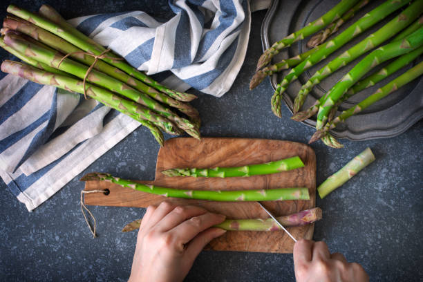 Fresh  raw asparagus on stone background. Women female hands cut asparagus on wooden cooking board. Top view stock photo