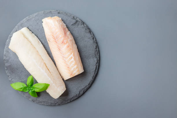 Fresh raw cod fillet with basil on stone plate, horizontal, copy space, top view stock photo