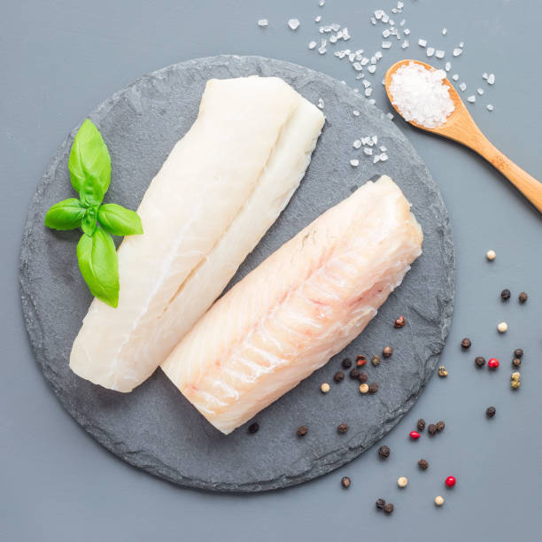 Fresh raw cod fillet with spices, pepper, salt, basil on a stone plate, top view, square format stock photo