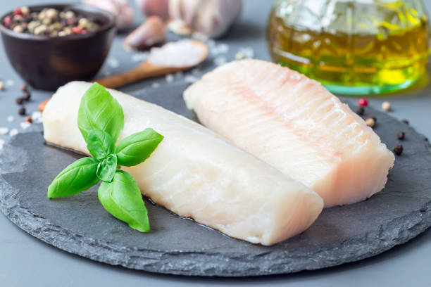 Fresh raw cod fillet with spices, pepper, salt, basil on stone plate, horizontal stock photo