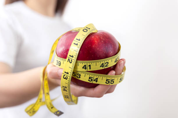 Fresh red apple with a measuring tape in female hands, close-up. Close-up of a red fresh apple with a measuring tape in female hands, the concept of weight loss, healthy eating. obesity stock pictures, royalty-free photos & images