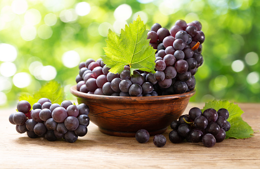 fresh ripe grapes with leaves in a bowl on a wooden table