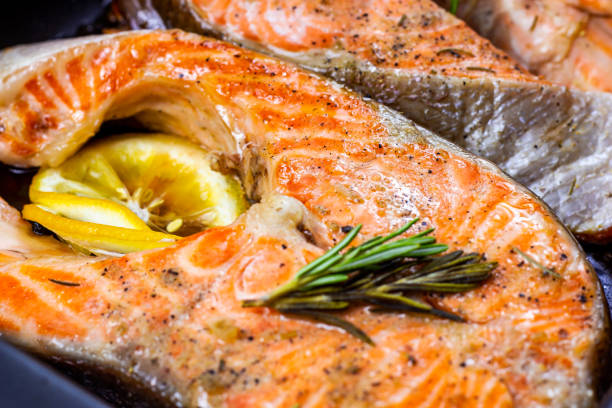 Fresh roasted red salmon fish steaks with herbs, spices and lemon on black metal plate background in the kitchen stock photo
