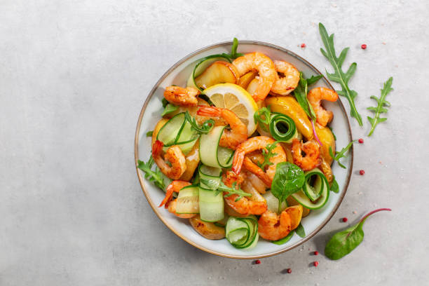 Fresh salad with grilled prawns, caramelized pears, cucumber and mixed greens, with lemon dressing.  Light grey background. Top view. stock photo