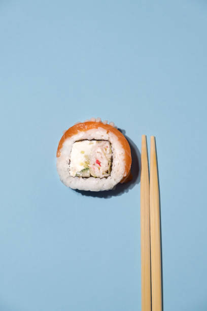 Fresh salmon sushi with wooden chopsticks on blue background. Sushi roll with chopsticks. Fish sushi roll. stock photo