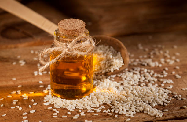 Fresh sesame oil in a glass bottle and seeds in a wooden spoon stock photo