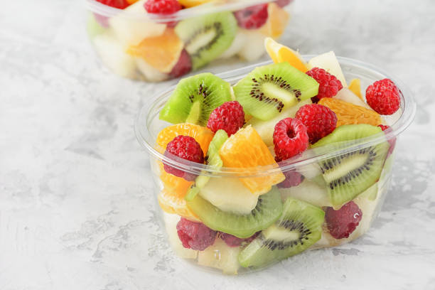 Fresh Sliced Tropical Fruits Berries in Container. Delicious Healthy Snack Ready to Eat Salad in Transparent Cup Closeup Elevated View. Vegetarian Raw Food. Citrus, Kiwi, Raspberries for Lunch stock photo