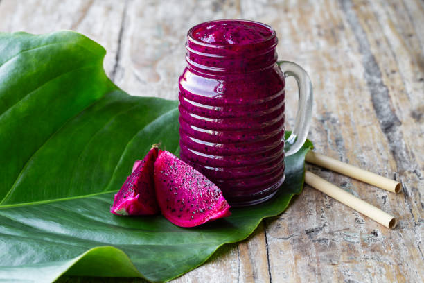 Fresh smoothie juice from a Dragon fruit (pitahaya) in a glass jar, fruit slices, tropical green leaf on old rustic table. stock photo