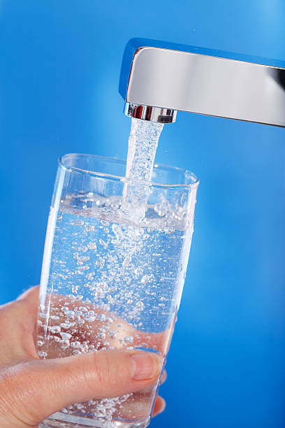 Fresh tap water filling a glass against a blue background stock photo