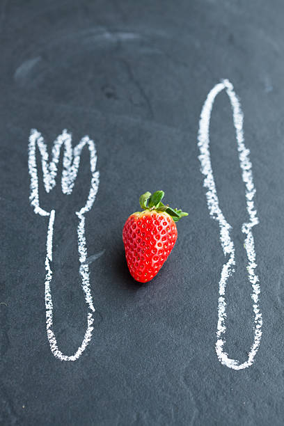 One fresh whole strawberry and chalk drawings of knife and fork on...