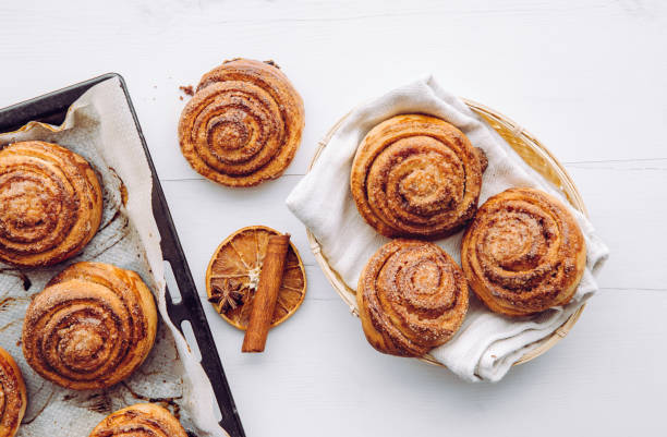 Freshly baked homemade cinnamon rolls in basket and on oven pan in the morning indoors, breakfast concept. Above view. stock photo