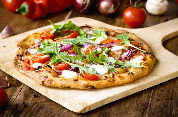 freshly baked pizza with arugula, tomato, red onion and mozzarella - pizza table imagens e fotografias de stock