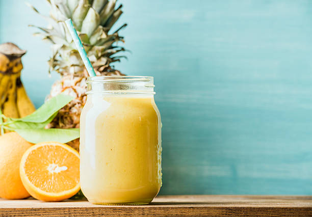 Freshly blended yellow and orange fruit smoothie in glass jar Freshly blended yellow and orange fruit smoothie in glass jar with straw. Turquoise blue background, copy space smoothie stock pictures, royalty-free photos & images