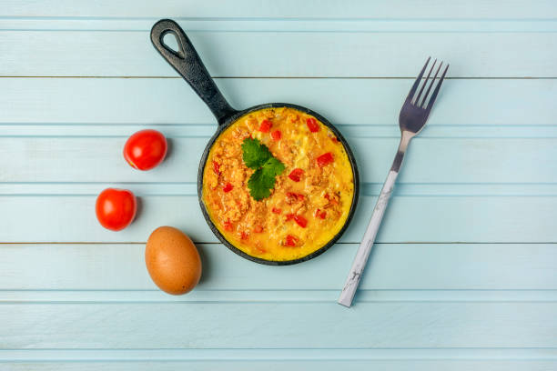 Freshly made omelet, Turkish national recipe Menemen with eggs, bell pepper and tomatoes. Photo on a blue background with copy space. stock photo