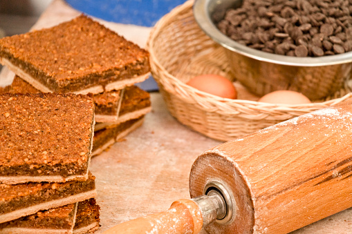 Freshly prepared nut wedges between a rolling pin, a bowl with chocolate beans and a basket with eggs on the work table in a bakery.