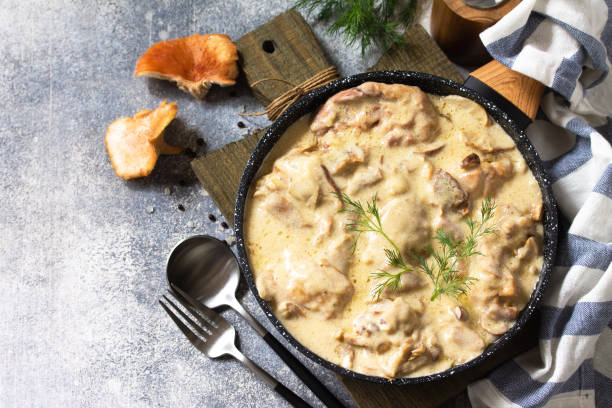 Fricasse - French Cuisine. Chicken stewed in a creamy sauce with mushrooms in a pan on a light stone background. Copy space. stock photo