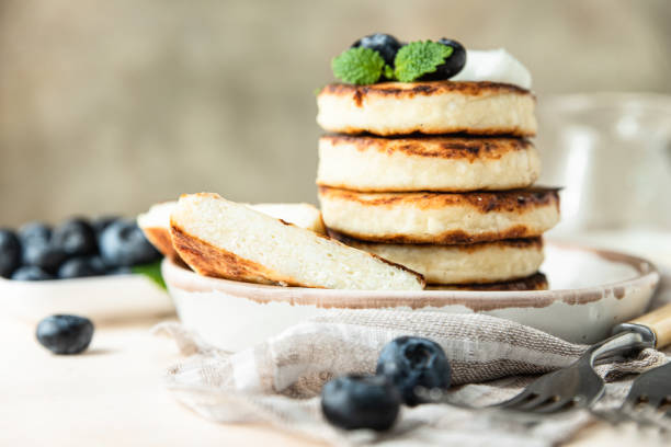Fried cottage cheese pancakes or fritters with blueberry and sour cream on a plate. Gluten free. Traditional breakfast of Ukrainian and Russian cuisine. stock photo