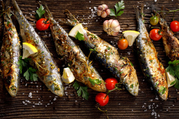 Fried fishes with addition of herbs, spices and lemon slices on a wooden background. stock photo
