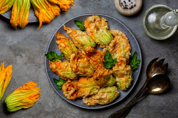 Fried in a batter Zucchini Flowers stuffed with ricotta cheese and parsley. Raw and Roasted courgette or pumpkin flowers. Italian dish fiori di zucca in pastella. Gray background. stock photo